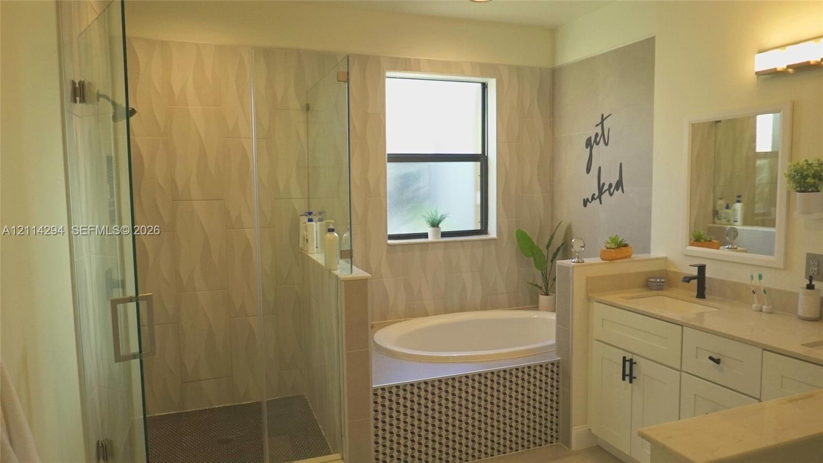 Bathroom featuring a glass-enclosed walk-in shower with textured wall tile, a deep soaking tub with geometric tile surround, white cabinetry, and a va