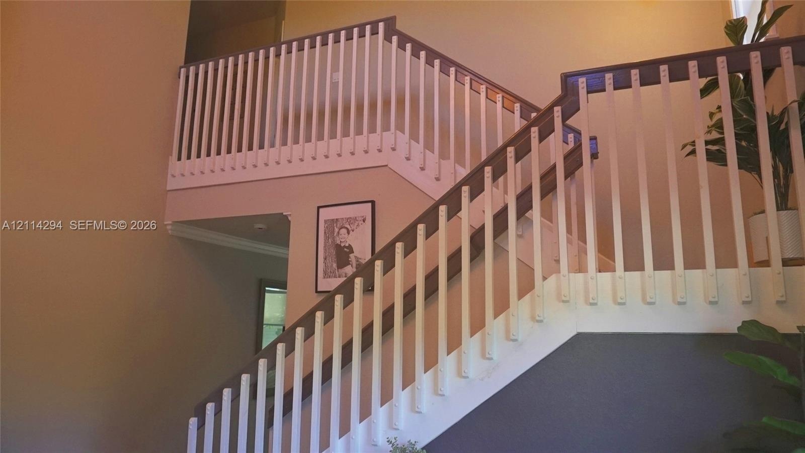 Staircase featuring a dual-toned wood handrail, vertical white balusters, and a high-ceiling configuration