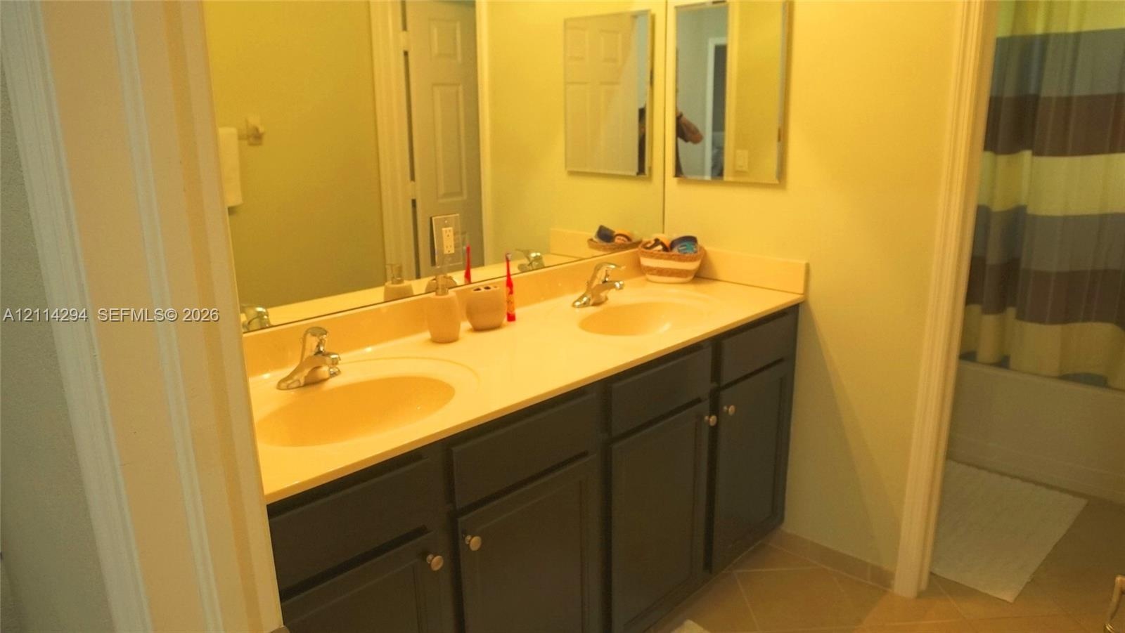 Dual-sink vanity featuring a solid surface countertop, dark-finish cabinetry, chrome-finish faucets, and an expansive wall-mounted mirror