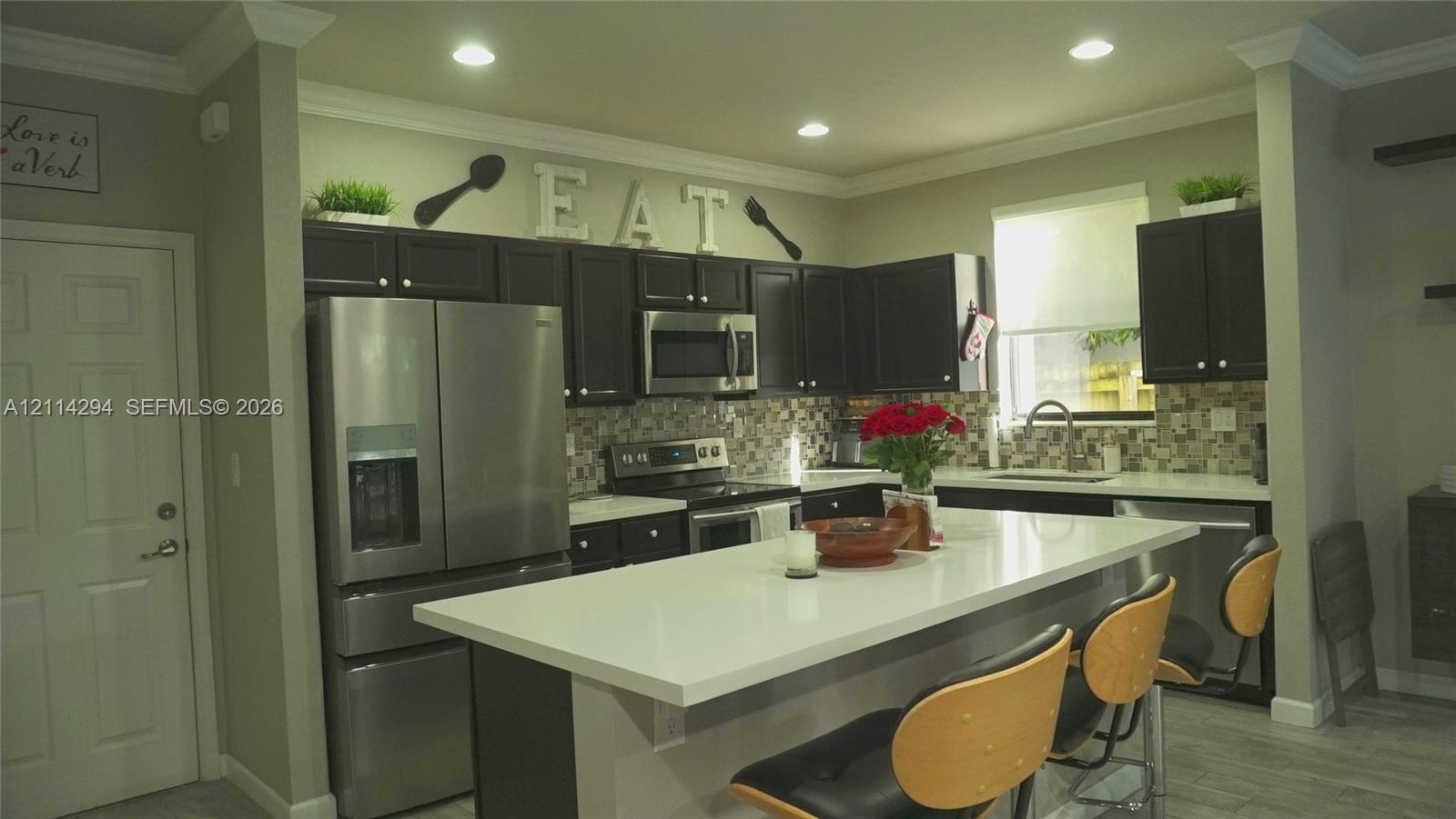 Kitchen featuring dark-finish cabinetry, a white countertop island, stainless steel appliances, a tile backsplash, and recessed lighting