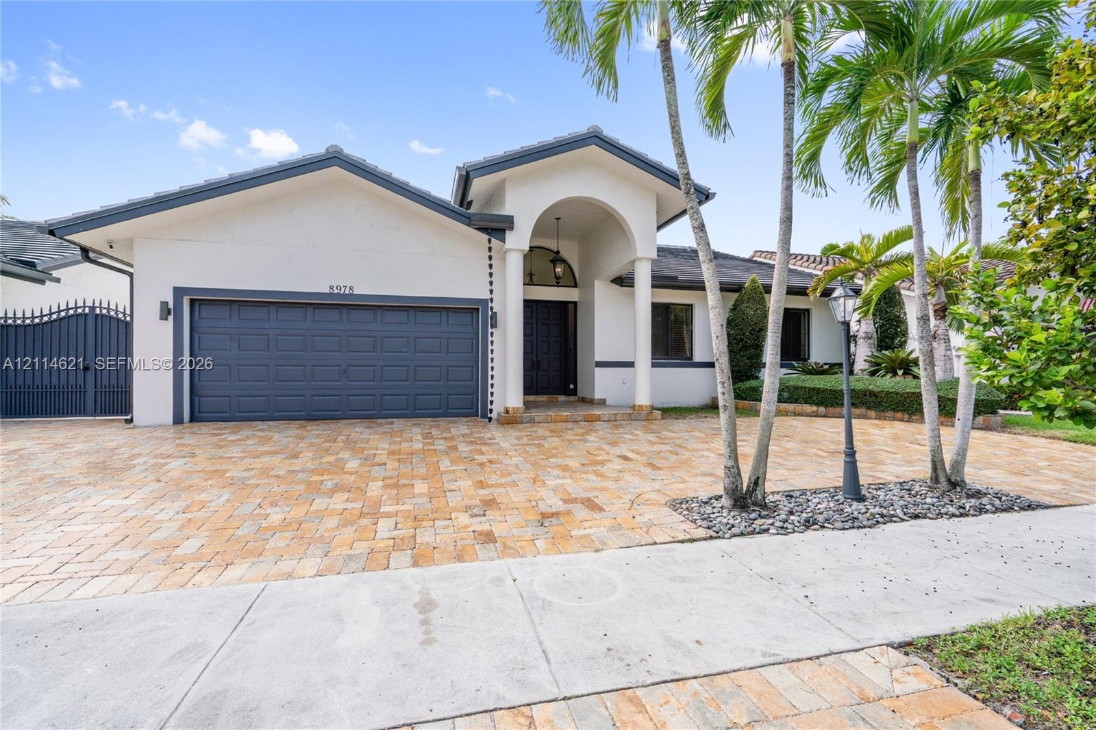 Single-story residence featuring a paver driveway, arched entryway, multi-panel garage door, and mature landscaping