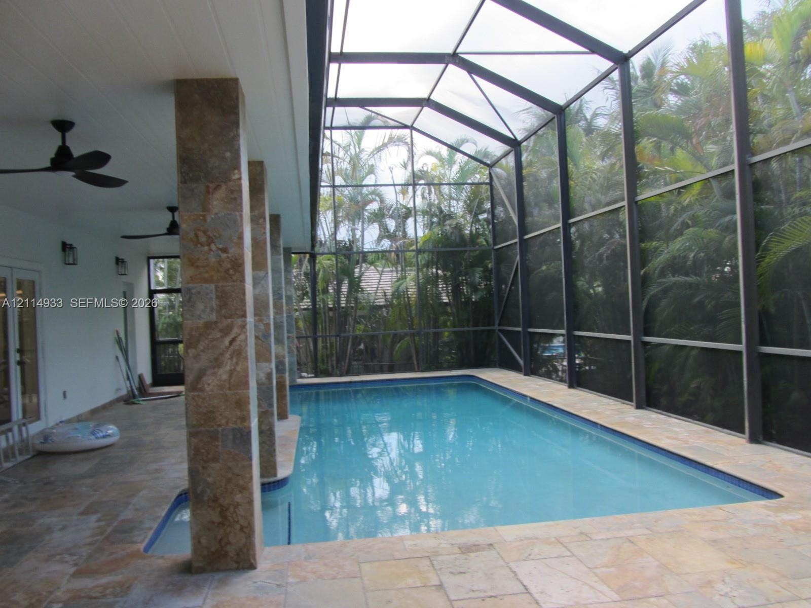 Screen-enclosed pool area featuring stone-tile decking, stone-clad structural pillars, recessed ceiling fans, and an attached covered patio
