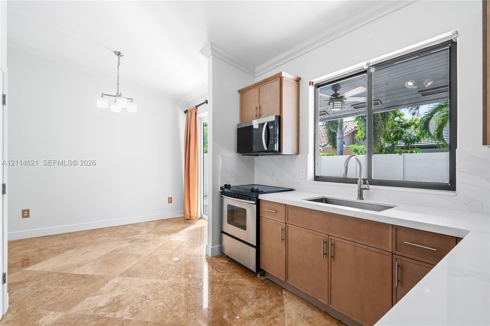 Kitchen featuring stone tile flooring, flat-panel wood cabinetry, quartz countertops, stainless steel appliances, and a stainless steel undermount sin