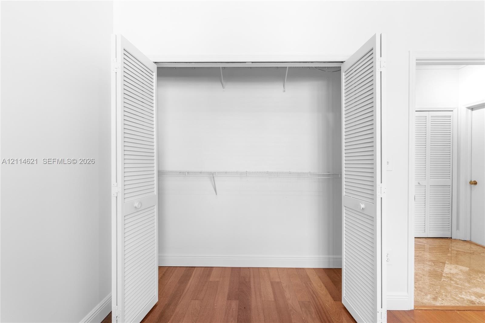 Storage area featuring dual white louvered bi-fold doors, wood-finish flooring, and integrated wire shelving
