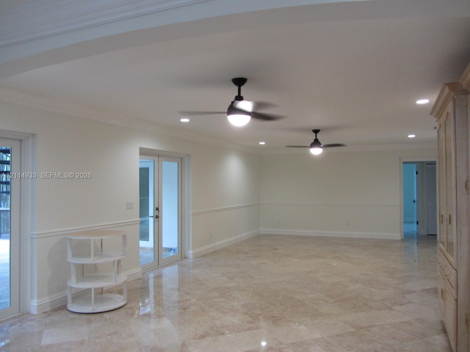 Polished stone flooring, crown molding, chair rail trim, dual ceiling fans with integrated lighting, and glass-paned French doors