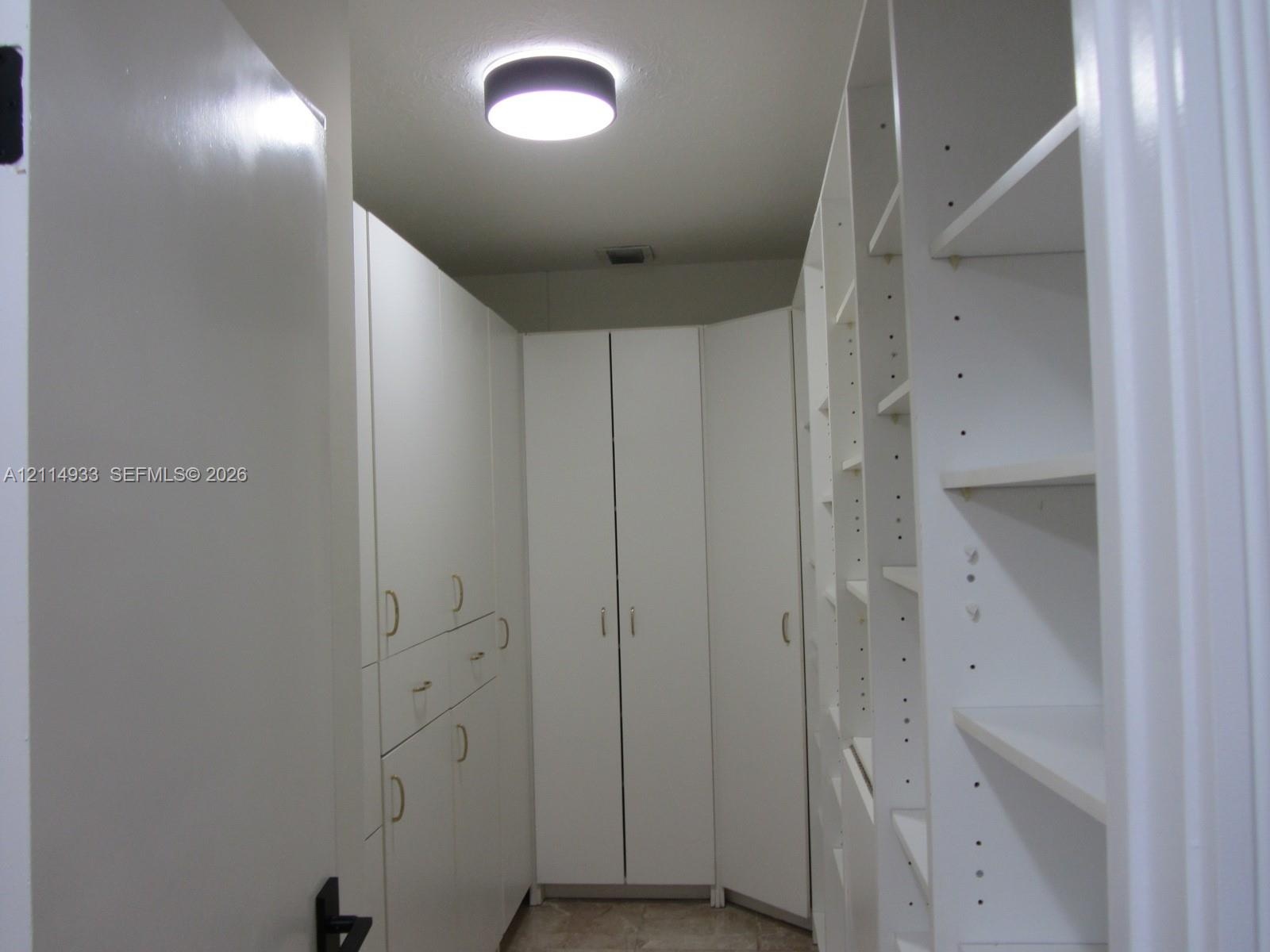Custom floor-to-ceiling cabinetry featuring white laminate finish, adjustable shelving, integrated storage drawers, gold-toned hardware, and a circula