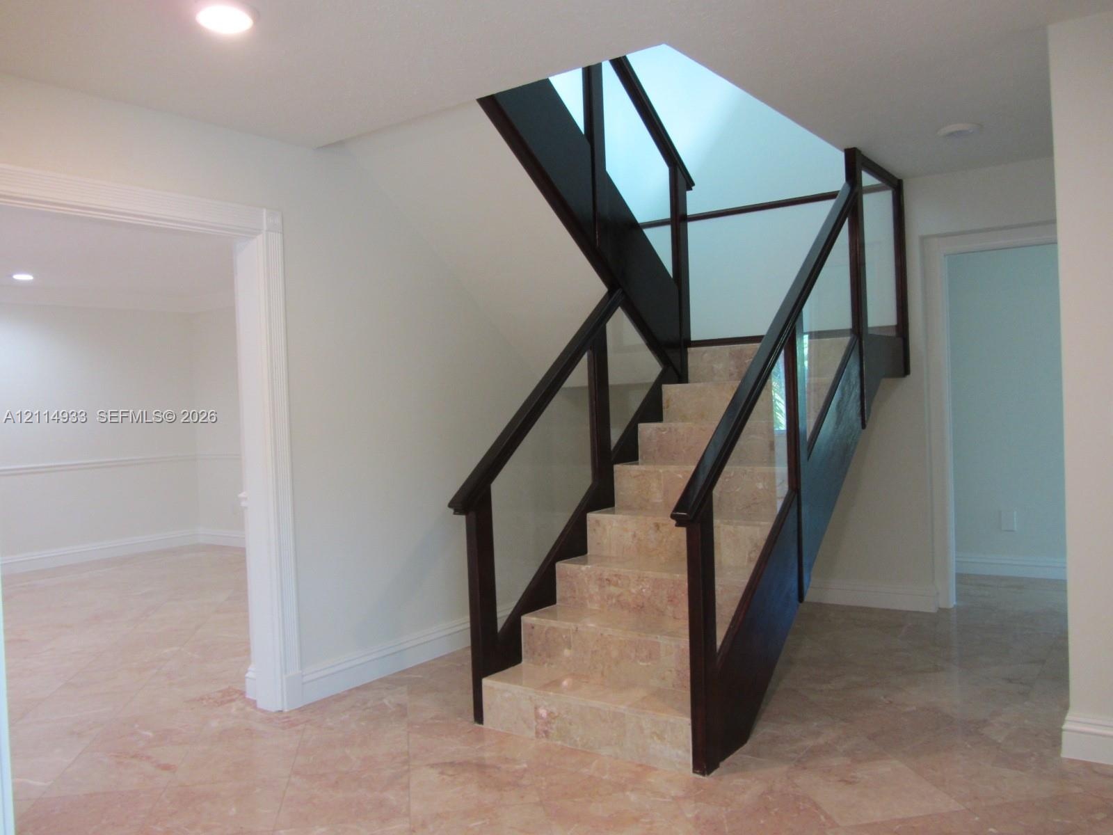 Staircase featuring natural stone treads, dark wood handrails, and glass panel balustrades beneath a skylight