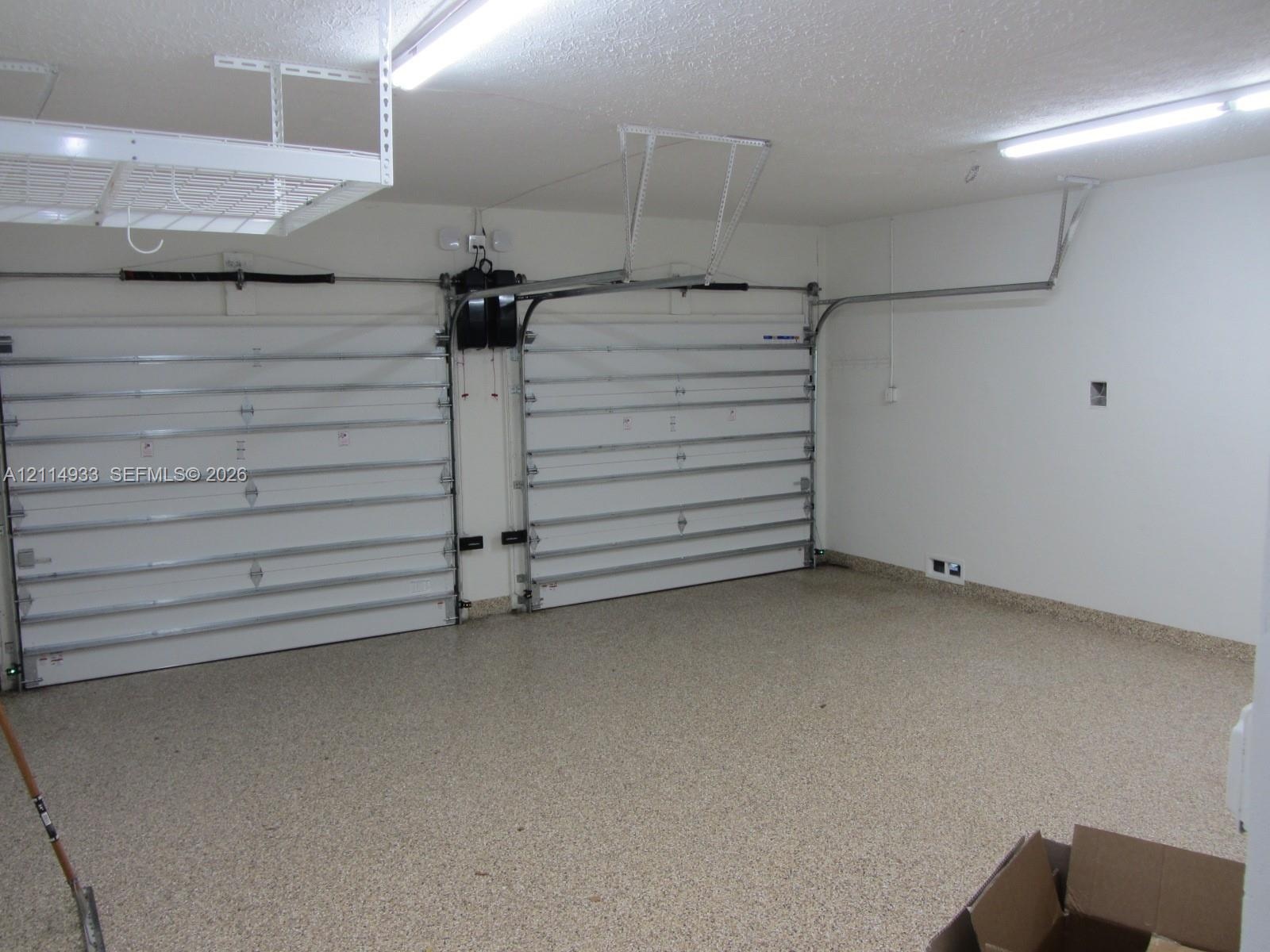 Two-car garage featuring dual overhead doors, overhead storage shelving, interior LED lighting, and speckled epoxy flooring