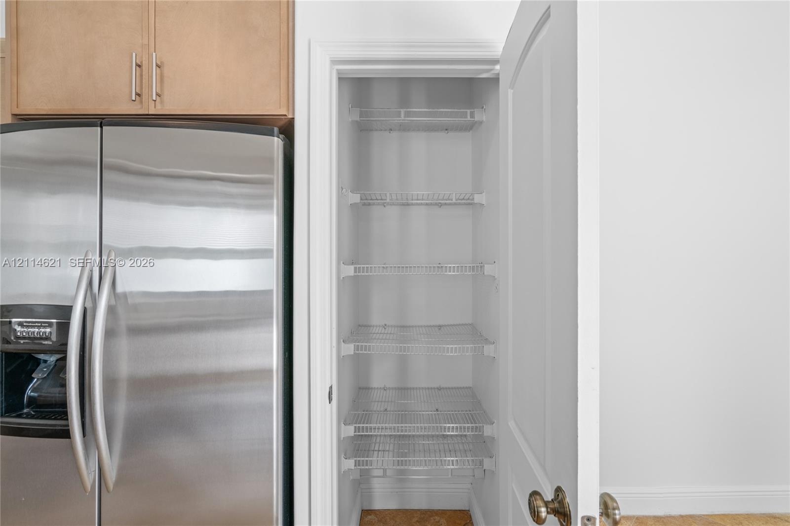 Pantry featuring multi-level wire shelving and a traditional hinged door, positioned beside stainless steel refrigeration and wood-finish cabinetry