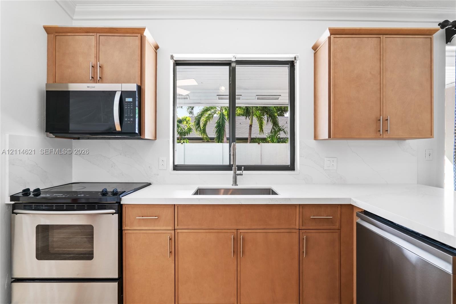 Kitchen featuring wood-finish cabinetry, solid surface countertops, a stainless steel undermount sink, matching stainless steel appliances, and a sing