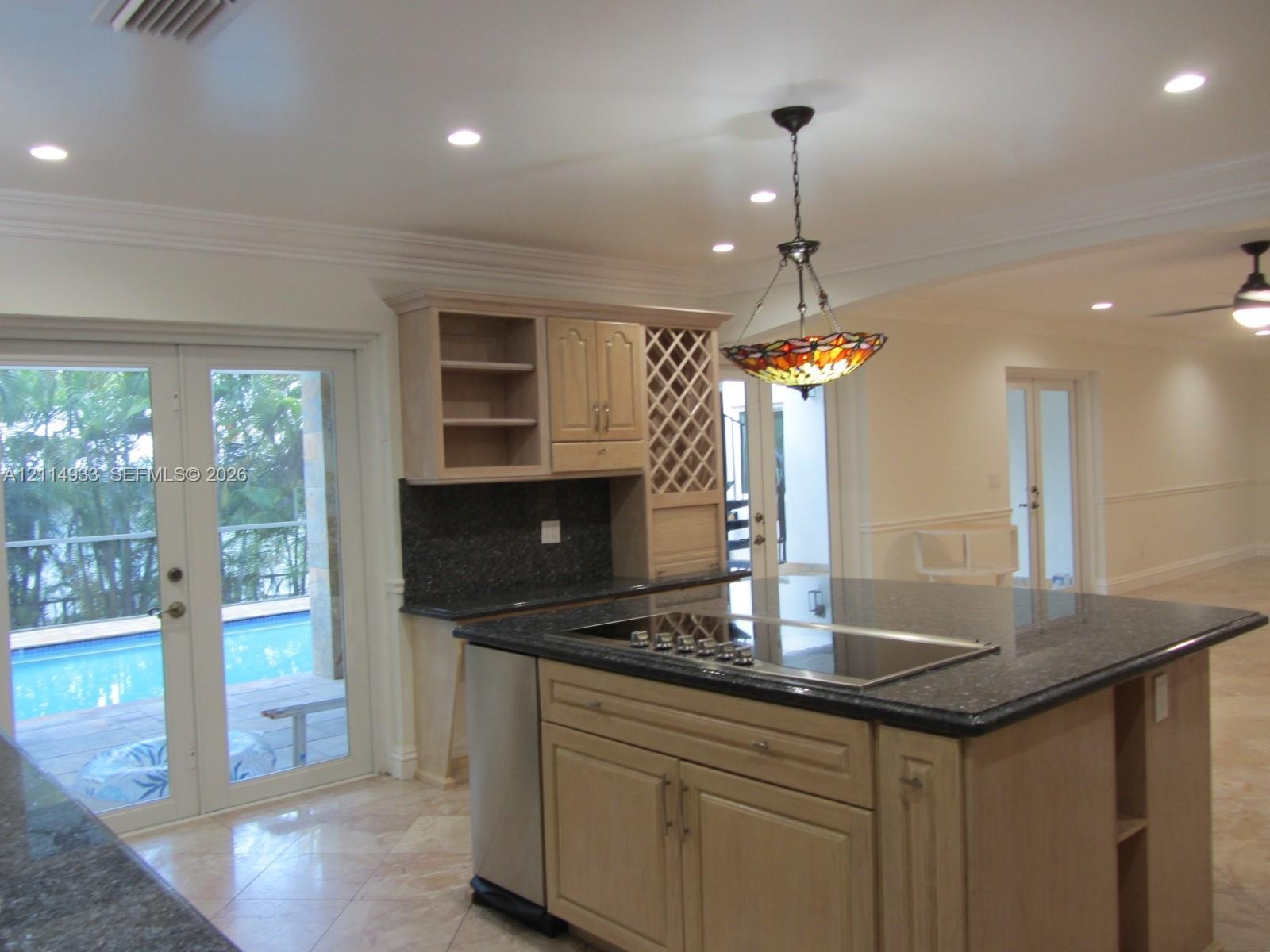 Kitchen featuring an expansive center island with a built-in cooktop, stone-finish countertops, custom wood cabinetry with integrated wine storage, an