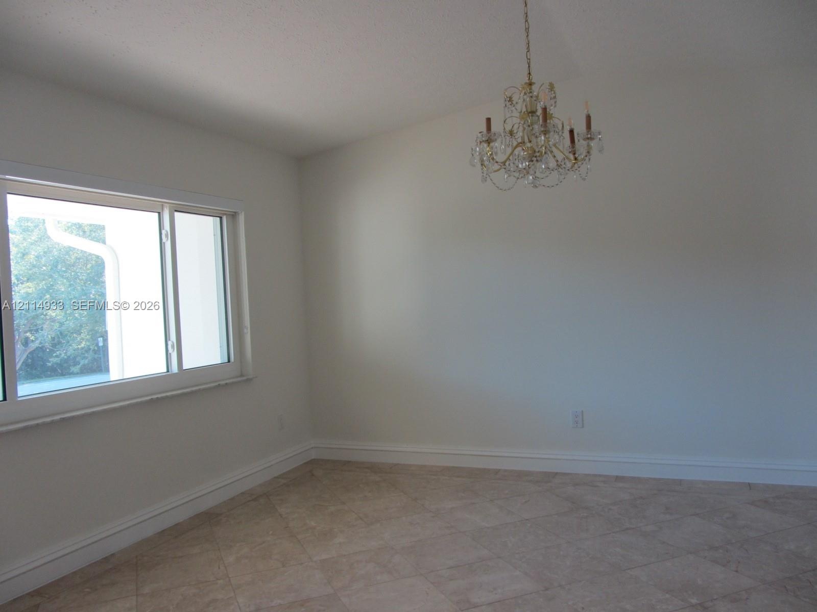 Vaulted ceiling, multi-light crystal chandelier, large-format tile flooring, and a wide horizontal window