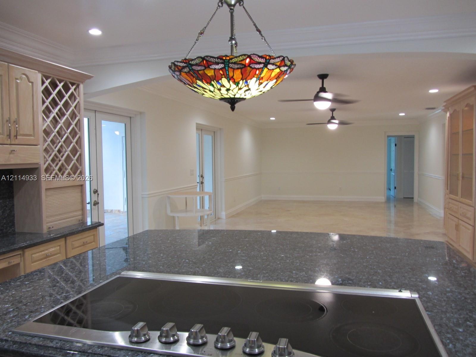 Kitchen featuring dark stone countertops, a glass-top cooktop, light wood cabinetry with built-in wine storage, recessed lighting, and a stained glass