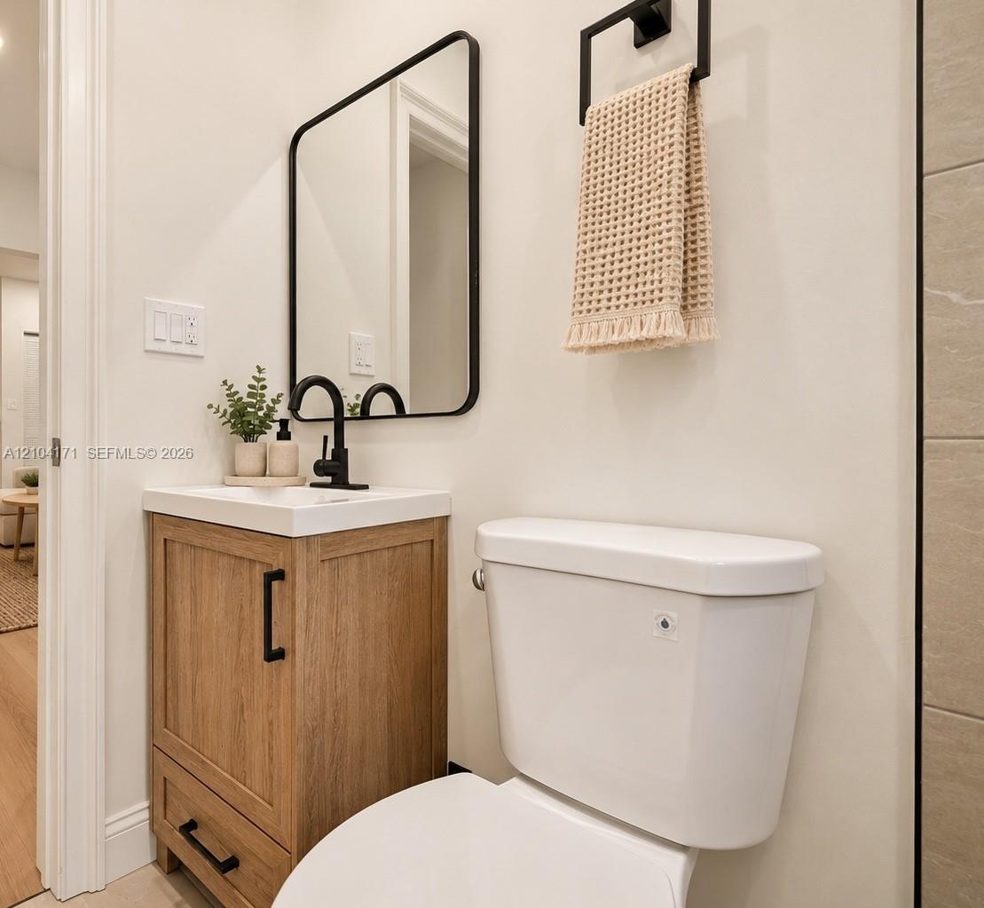 Wood-finish vanity with a rectangular sink, matte black faucet, rounded rectangular mirror, and matte black towel hardware