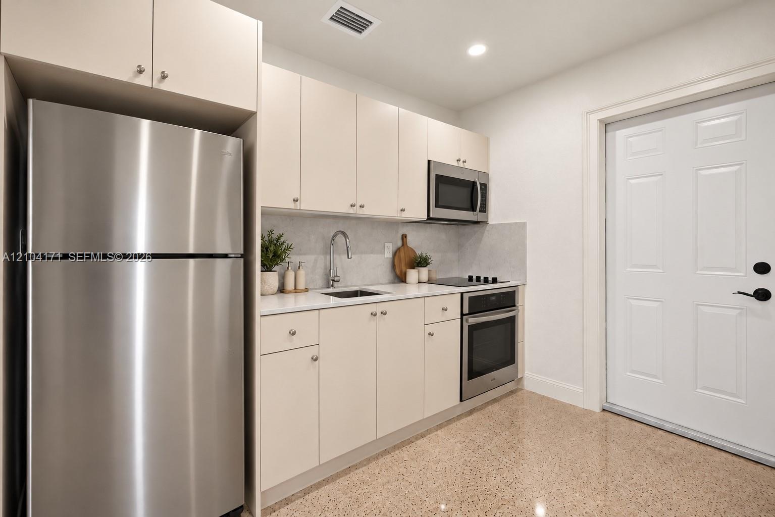 Kitchen featuring flat-panel cabinetry, quartz countertops, and stainless steel appliances including a refrigerator, built-in microwave, and electric 