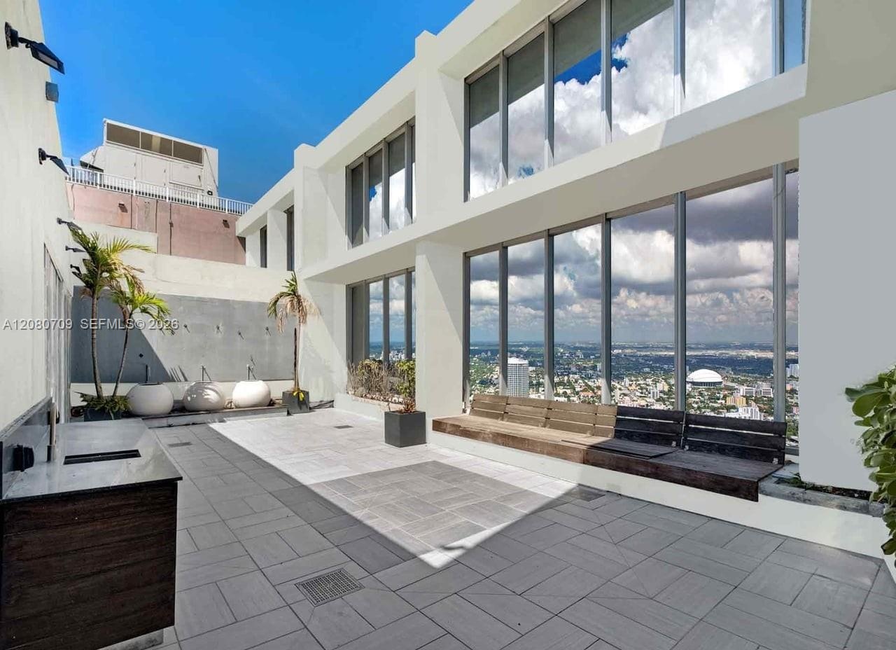 Expansive rooftop terrace featuring large-format tile flooring, floor-to-ceiling glass windows, a built-in outdoor kitchen with stone countertop, and 