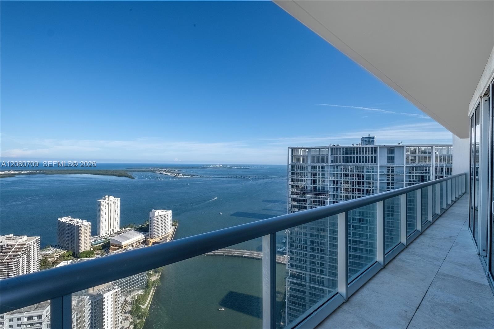 Floor-to-ceiling windows, wood-finish flooring, recessed lighting, and a private balcony with water and skyline scenery