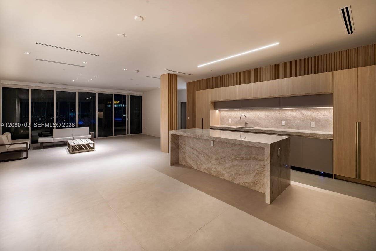 Kitchen featuring a waterfall island with natural stone surfaces, wood-finish cabinetry, under-cabinet lighting, and integrated linear lighting fixtur