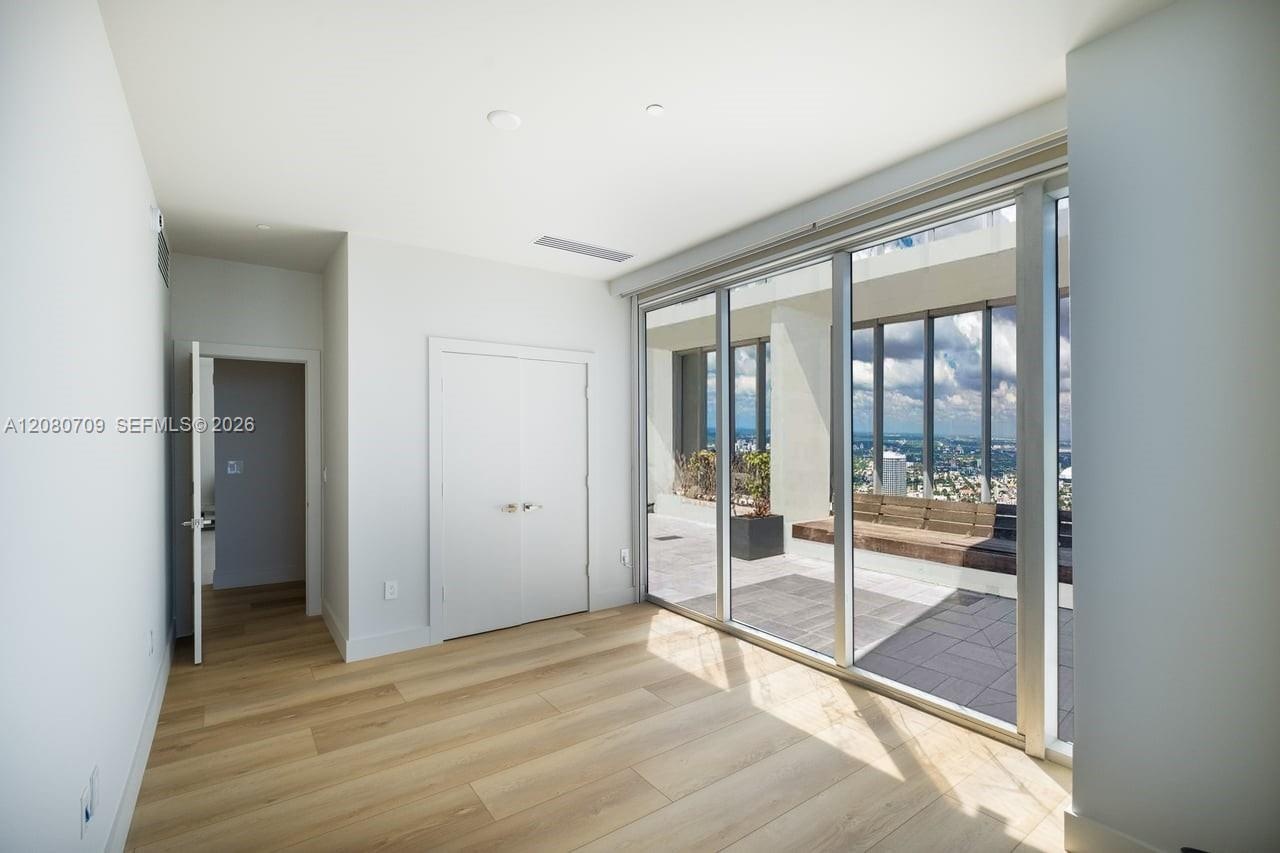 Minimalist interior featuring wood-finish flooring, floor-to-ceiling windows, and high-rise water and cityscape backdrops
