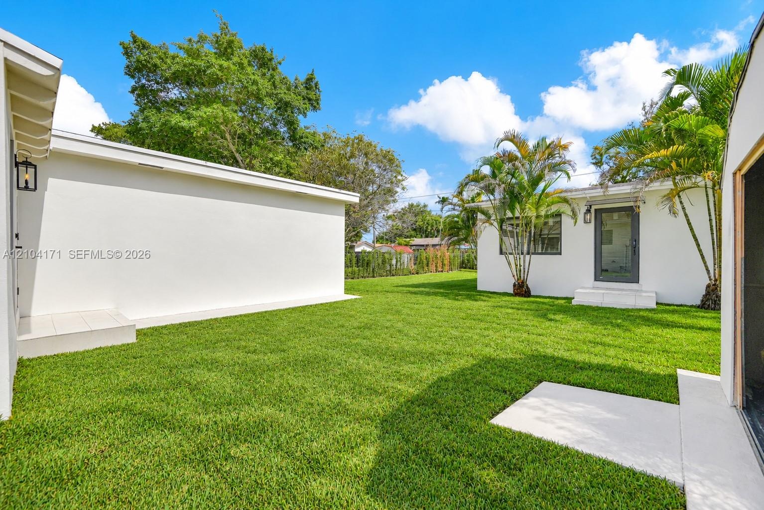Backyard featuring a manicured lawn, perimeter masonry wall, detached storage structure, concrete walkway, and exterior wall-mounted lighting
