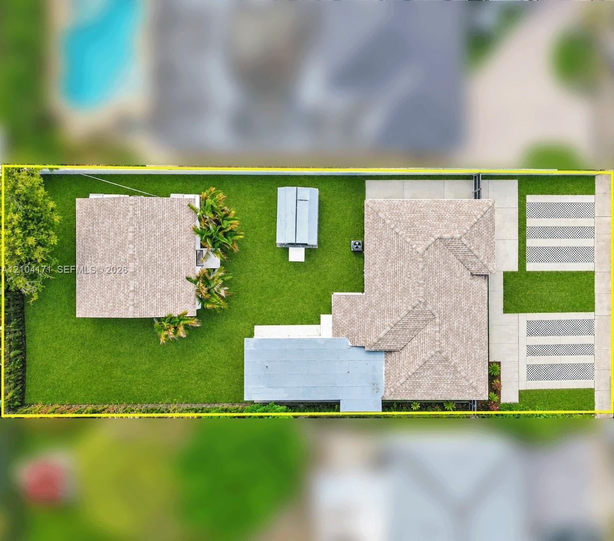 Aerial perspective featuring a white exterior residence, expansive lawn, multi-vehicle concrete parking area, and mature landscape