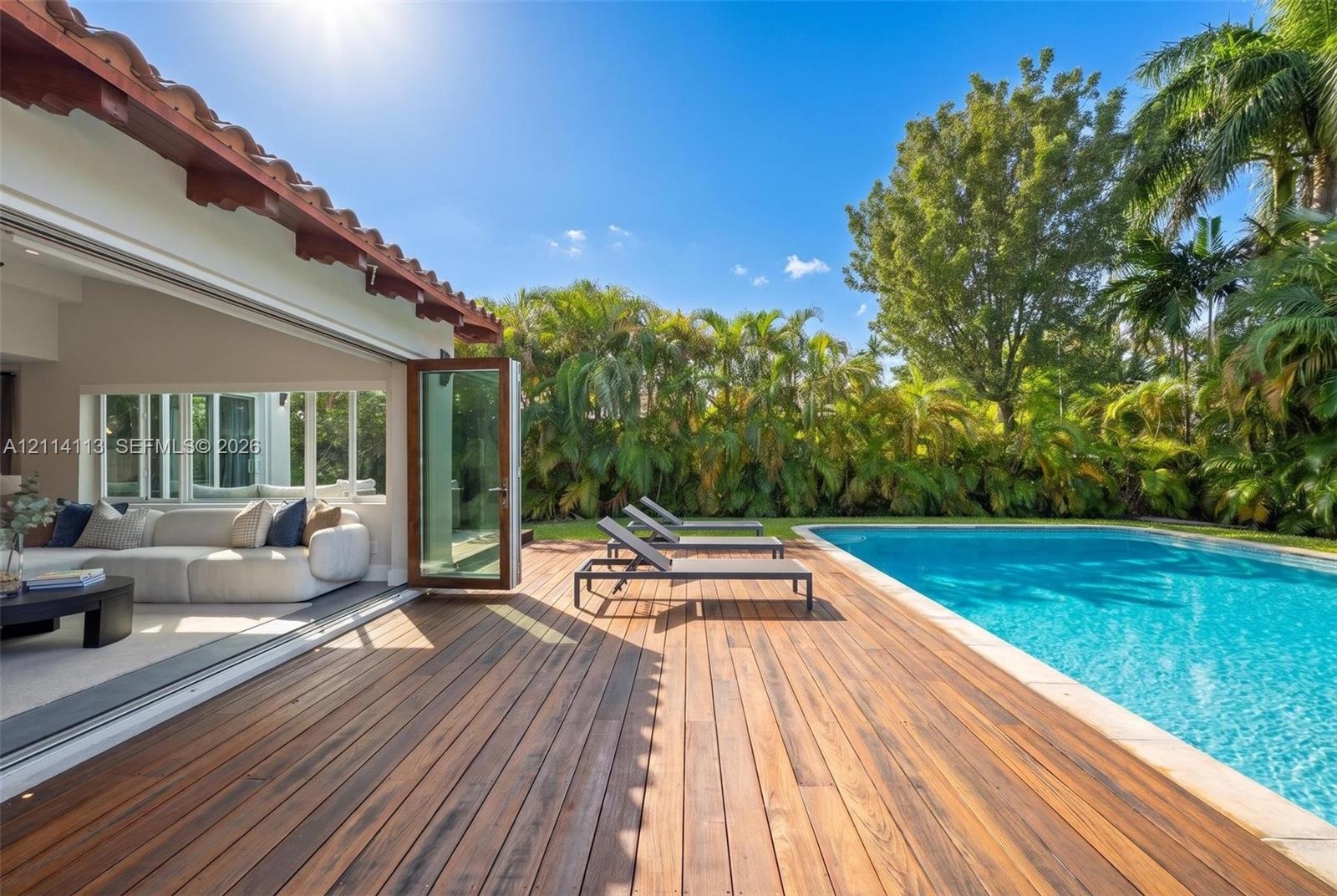Rear exterior featuring a wood-finish deck, swimming pool, and wide-opening glass panel doors