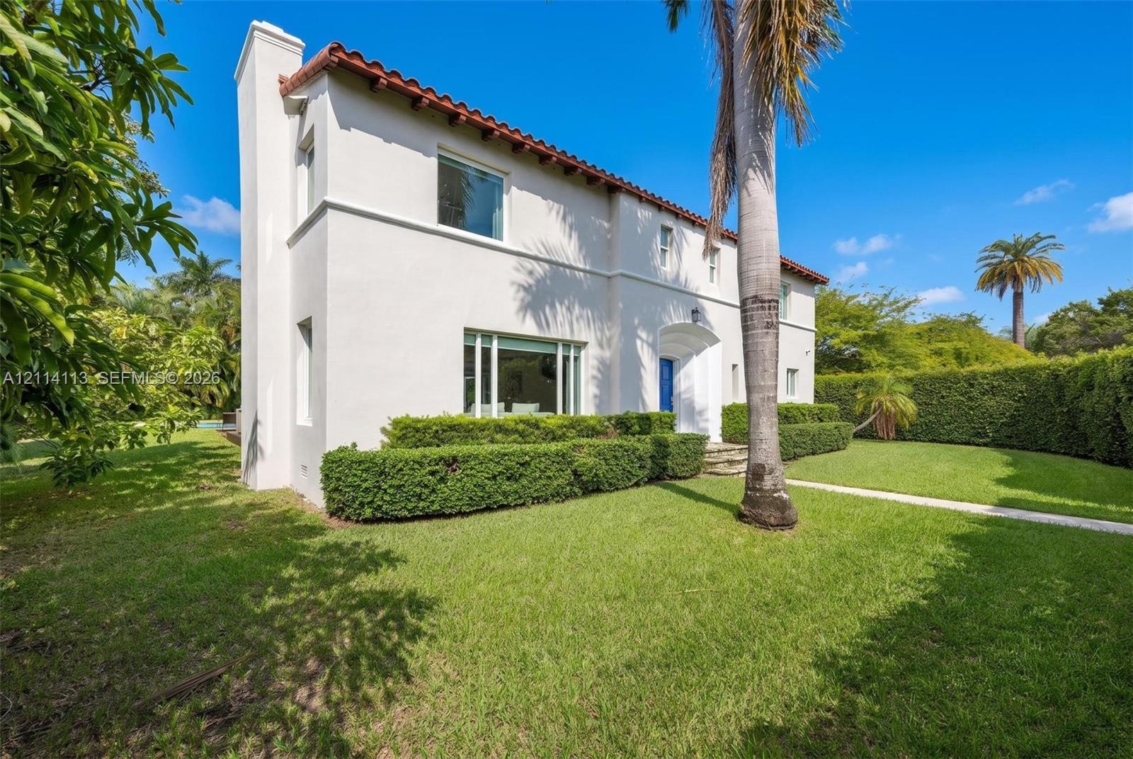 Stucco exterior featuring a clay tile roof, arched entryway, and manicured landscaping