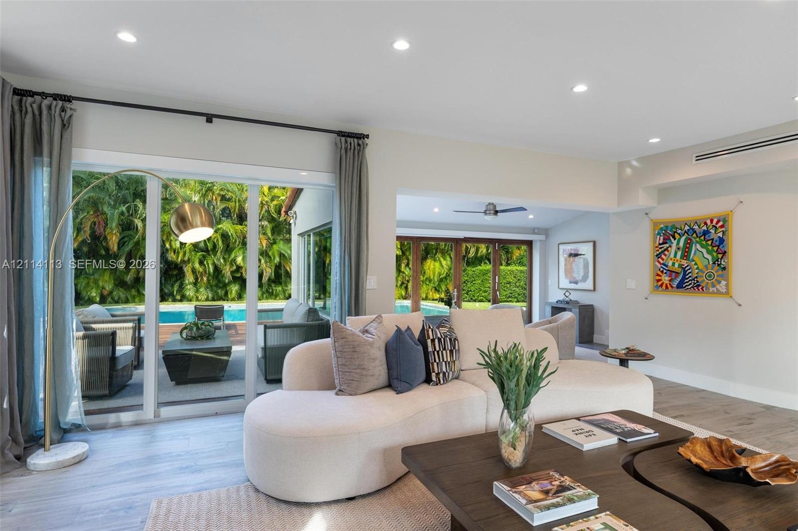 Living area featuring wood-finish flooring, recessed lighting, and multiple sliding glass door systems providing direct access to the outdoor pool are