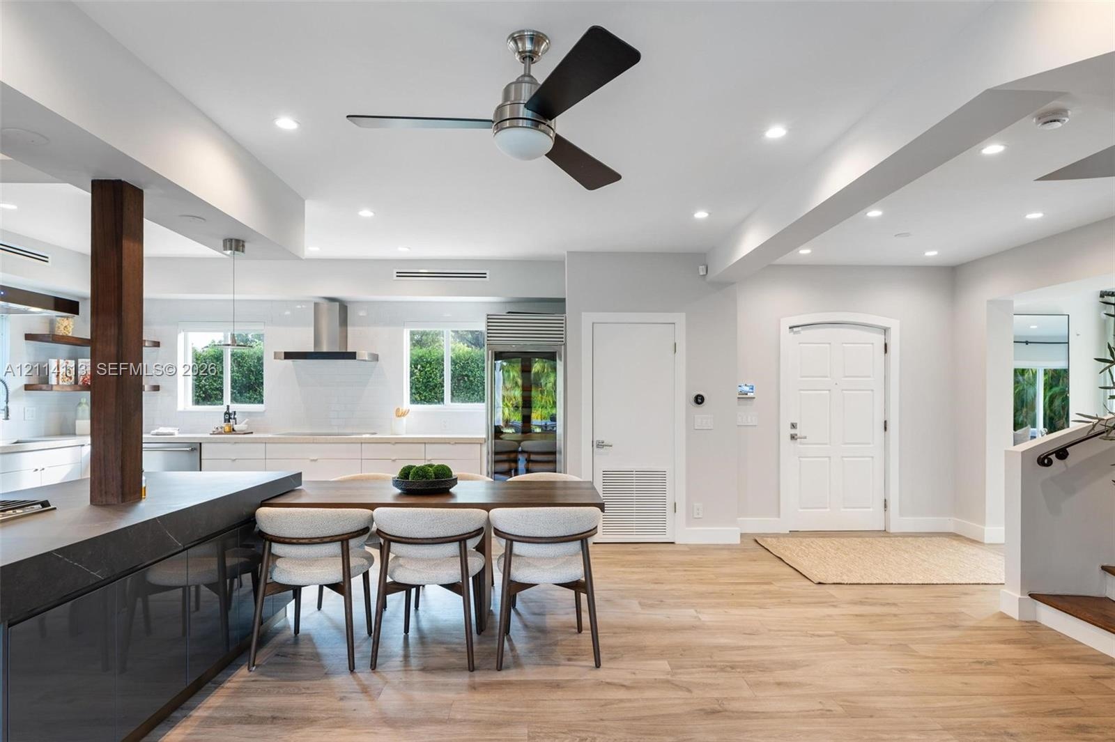 Open-concept interior featuring wood-finish flooring, recessed lighting, a modern ceiling fan, and a kitchen with a dark stone-top island and built-in