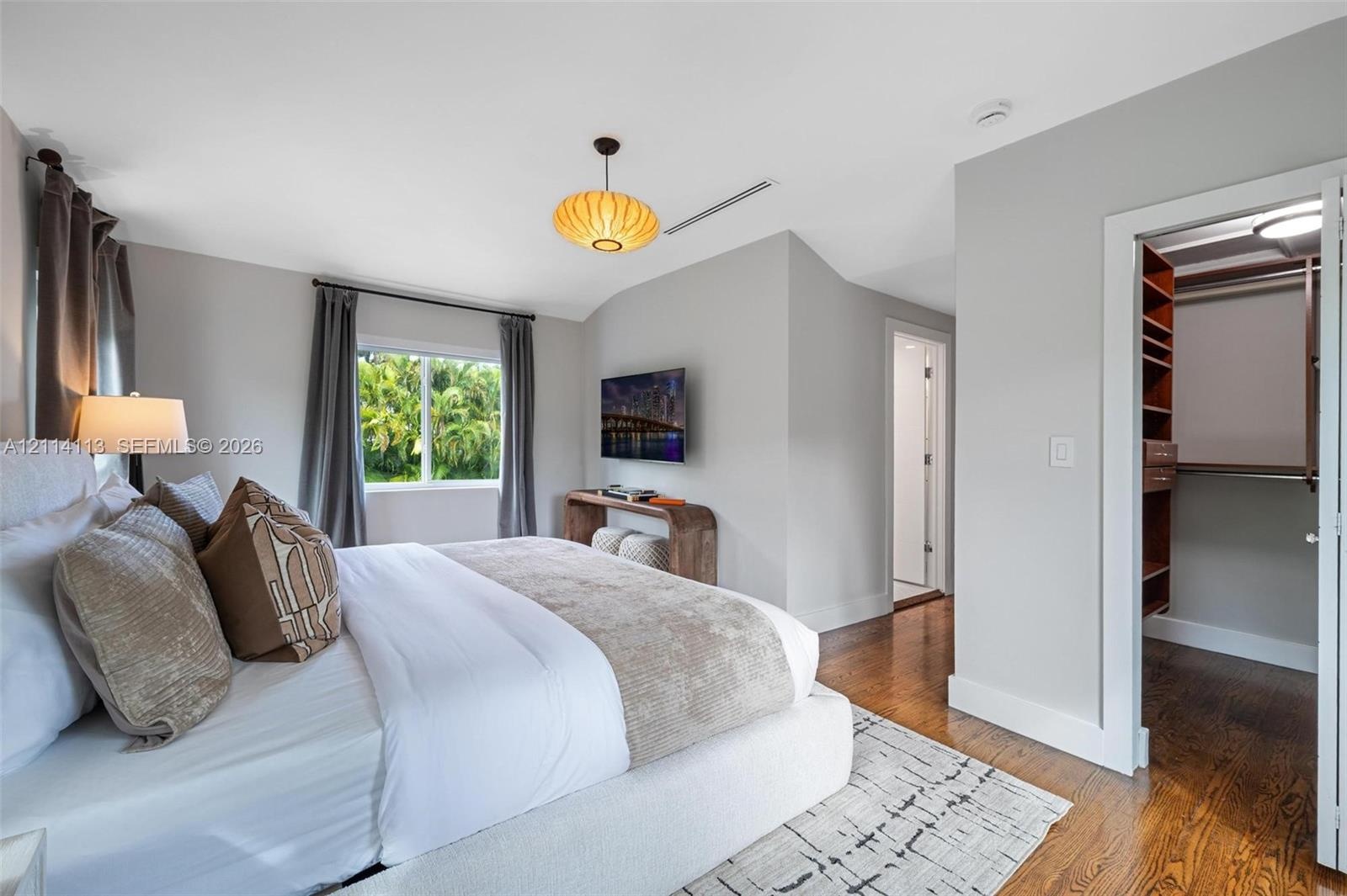 Natural wood flooring, custom built-in closet cabinetry and a window framing exterior foliage