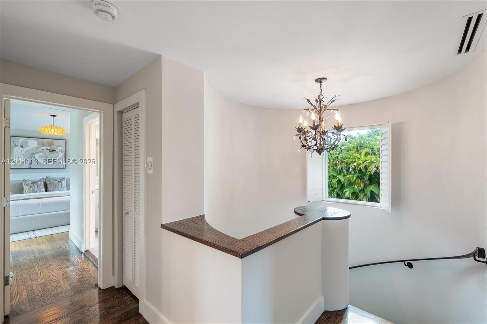 Curved architectural wall featuring a dark wood-finish cap, wrought-iron style chandelier, louvered closet door, and wood-finish flooring