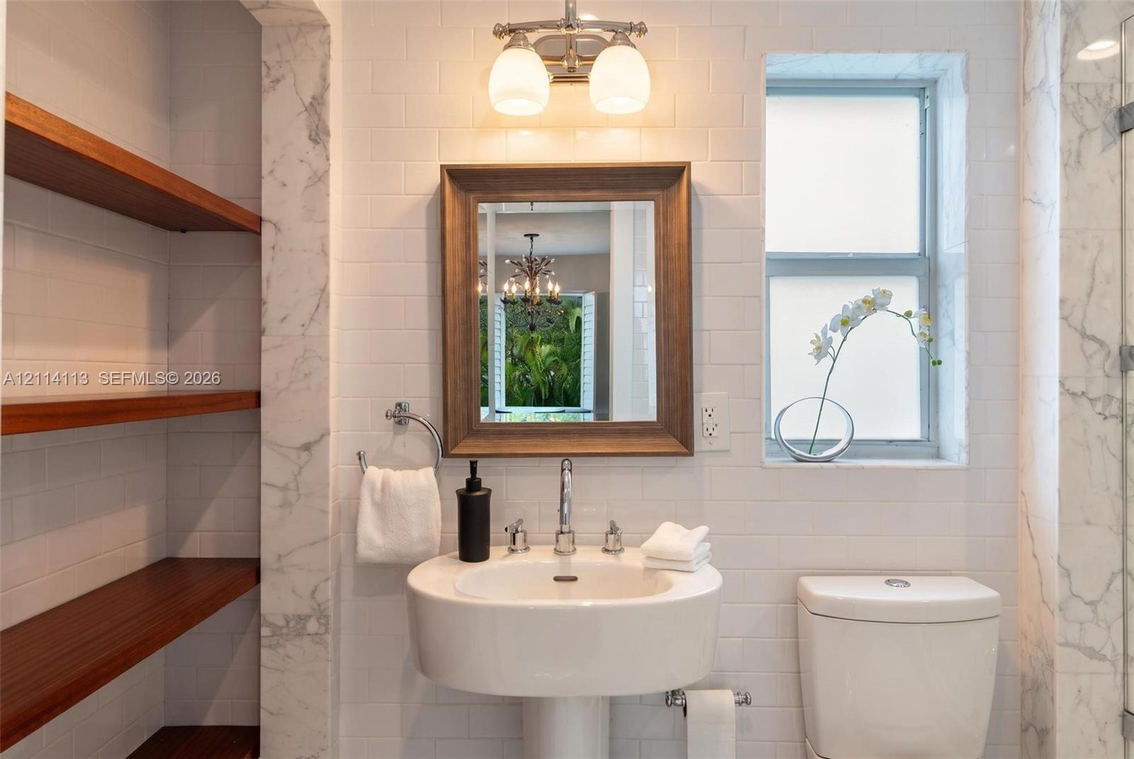 Bathroom featuring subway tile walls, stone-trimmed recessed shelving with wood-finish floating shelves, a pedestal sink with a chrome faucet