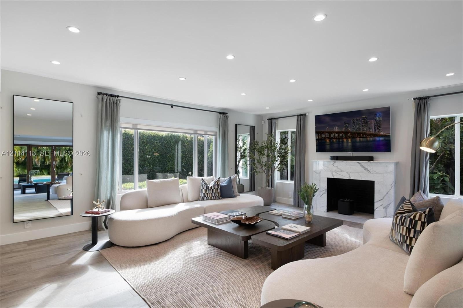 Spacious interior filled with natural light, featuring recessed lighting, stone-finish fireplace surround, large-format windows, and wood-finish porce