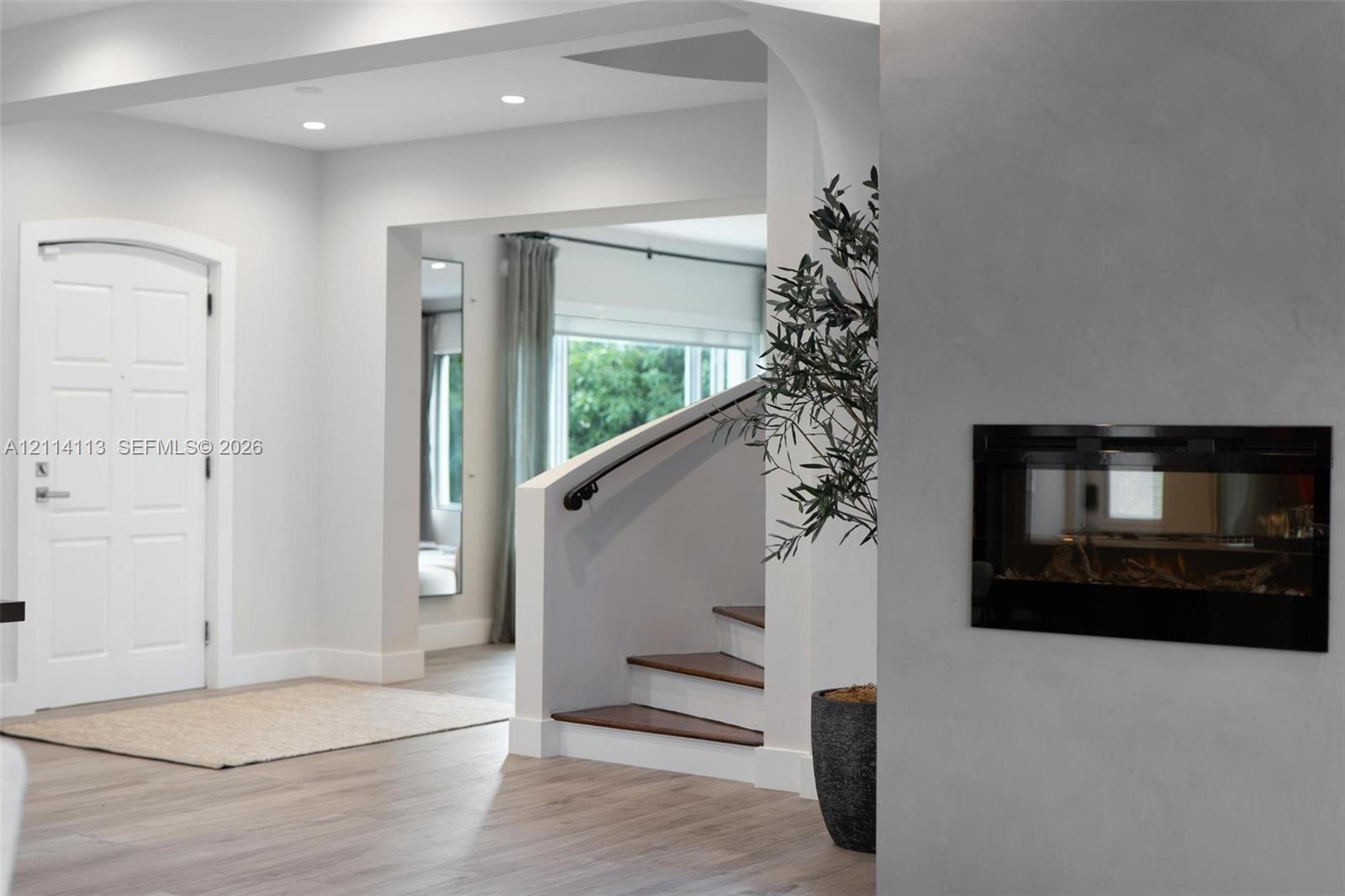 Foyer featuring recessed lighting, a recessed wall-mounted fireplace, a white arched-top entry door, and a staircase with wood-finish treads and a mat