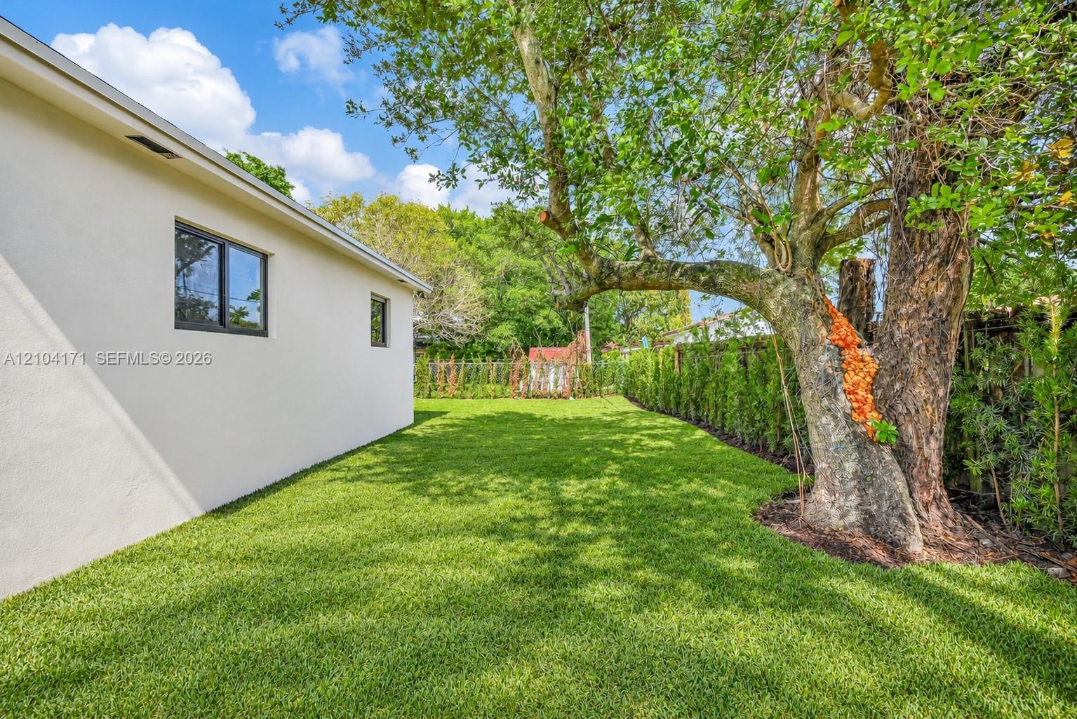 Private backyard featuring a manicured lawn, perimeter hedge landscaping, mature trees, and a chain-link fence