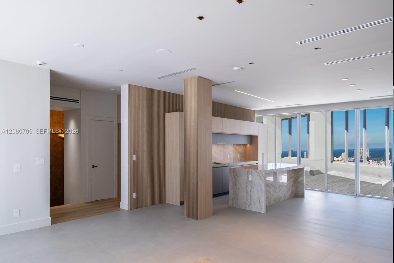 Custom kitchen featuring stone-slab waterfall island and countertops, natural wood-finish cabinetry, fluted wood wall paneling, and integrated under-c