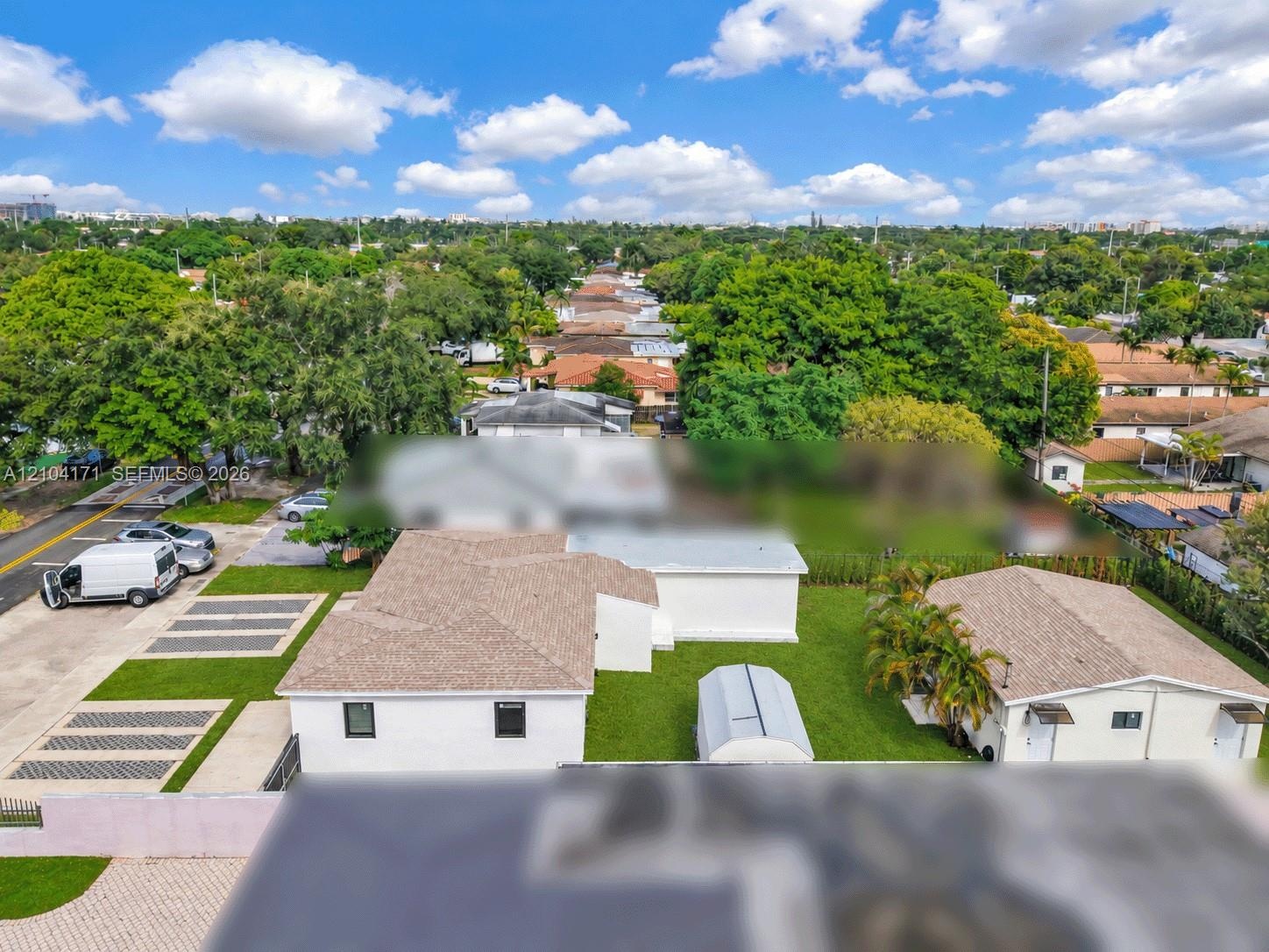 Aerial perspective featuring a single-story structure with a neutral-toned hip roof, paved multi-vehicle driveway, integrated lawn strips, and surroun