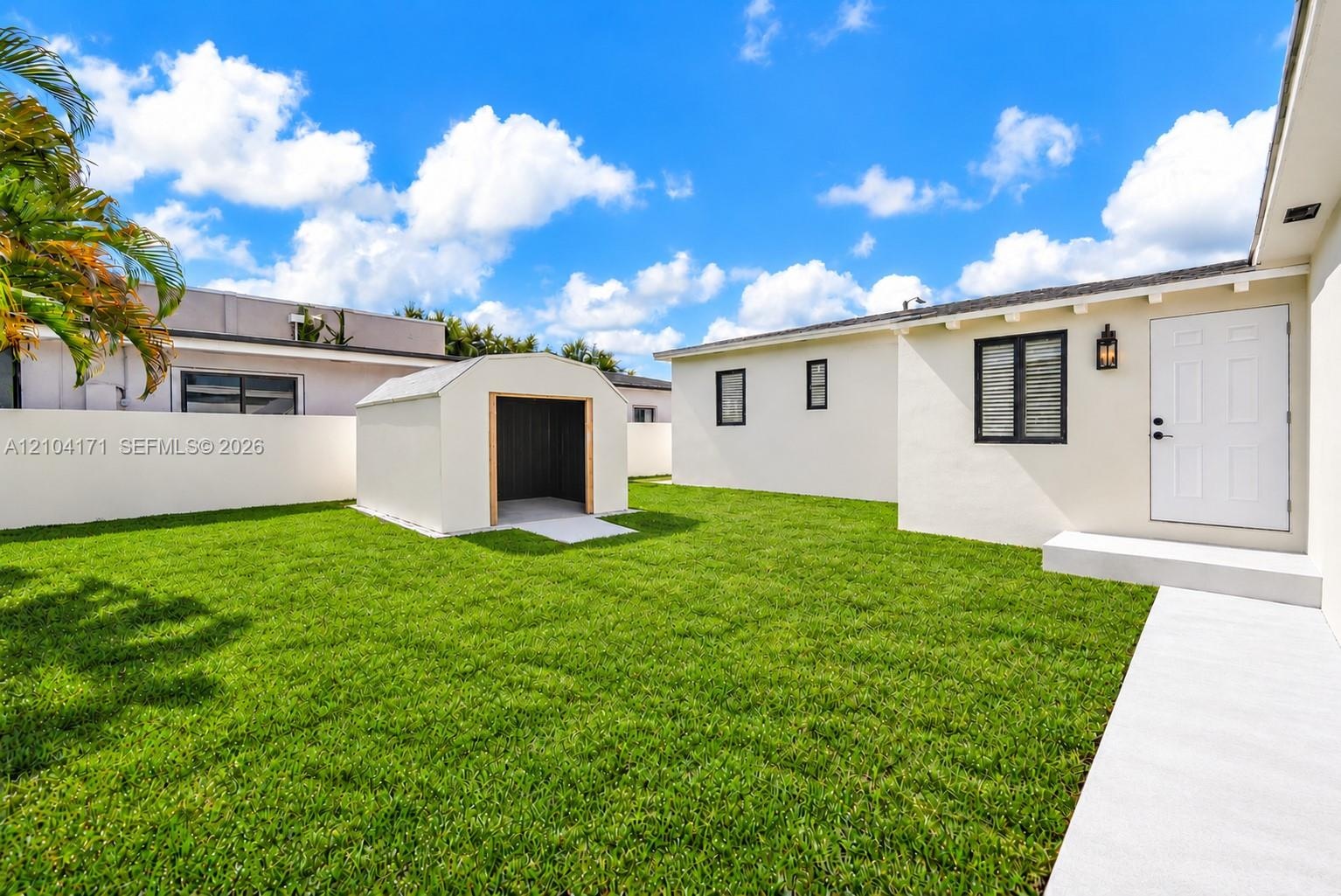 Aerial perspective featuring a manicured lawn, a detached structure, a paved driveway with turf ribbon accents, and perimeter landscaping