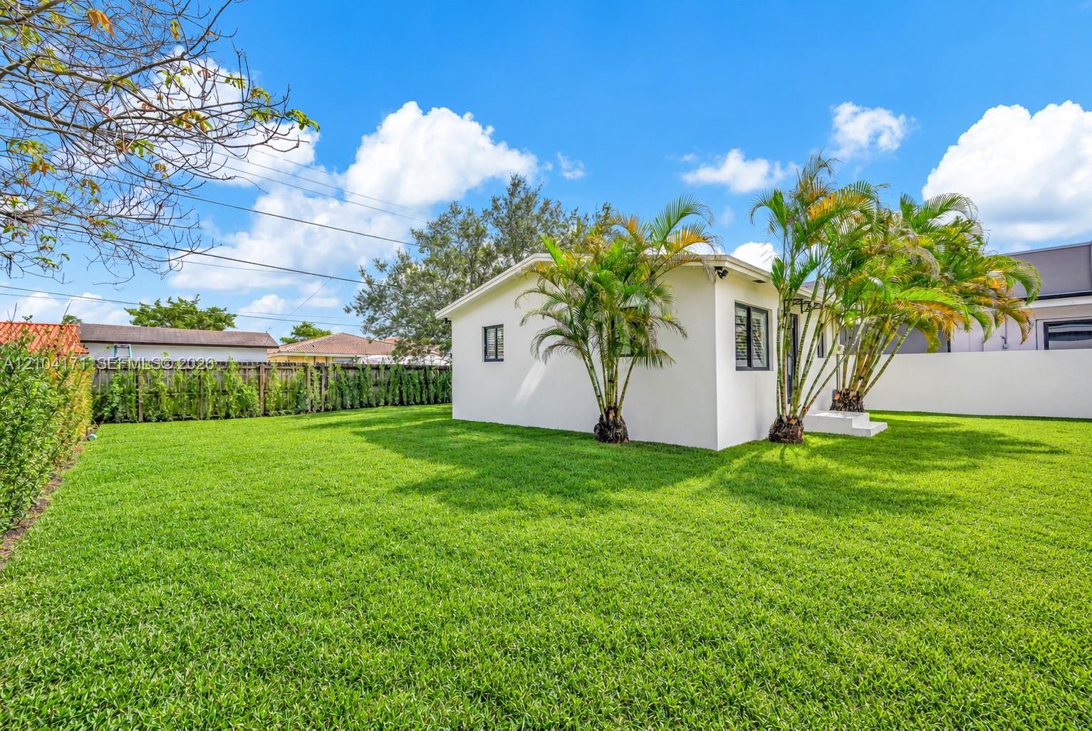 Expansive backyard featuring a manicured lawn, perimeter fencing, and mature palm trees