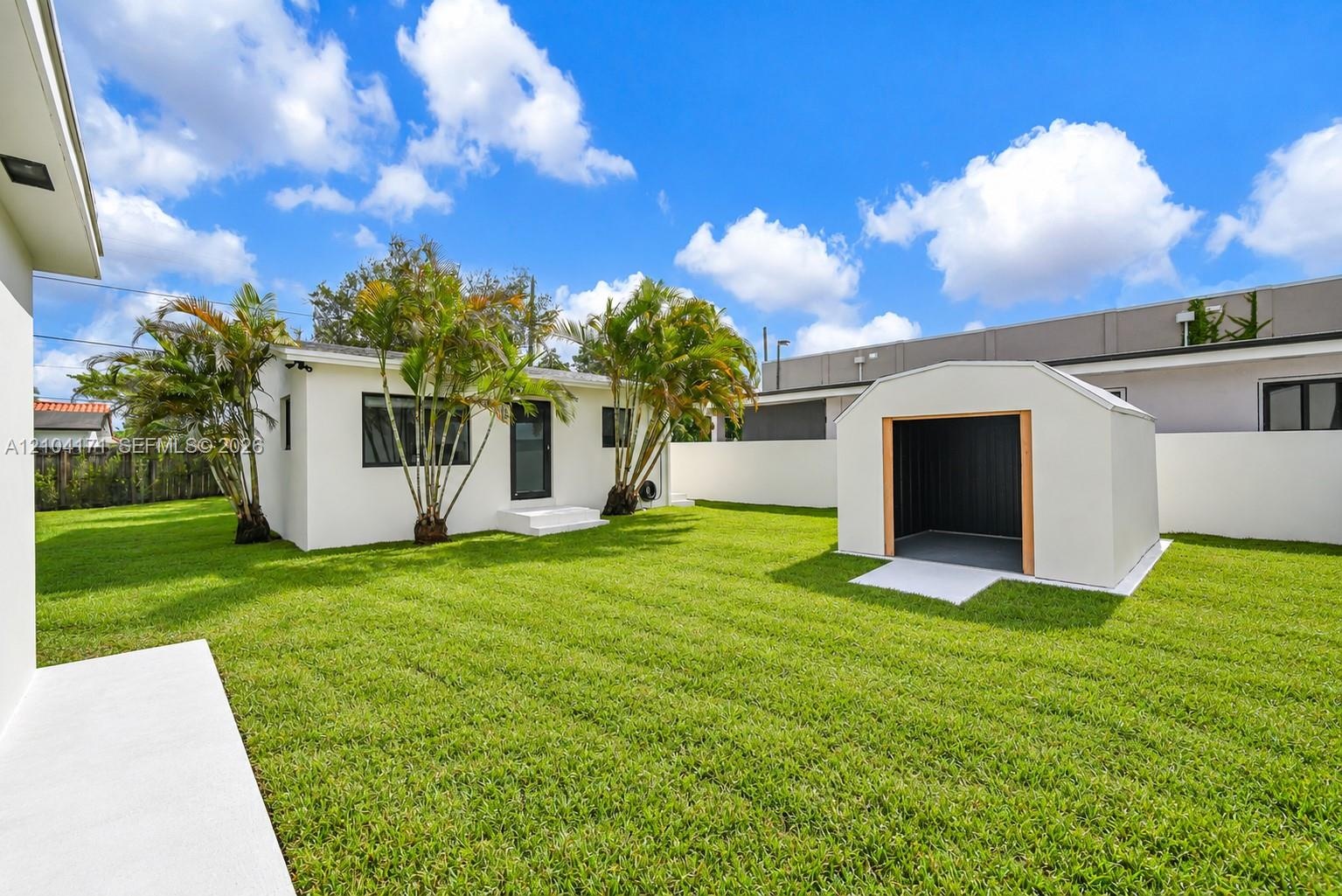 Aerial perspective of the property featuring white stucco exterior finishes, shingled roofing, expansive manicured lawn space, and mature trees