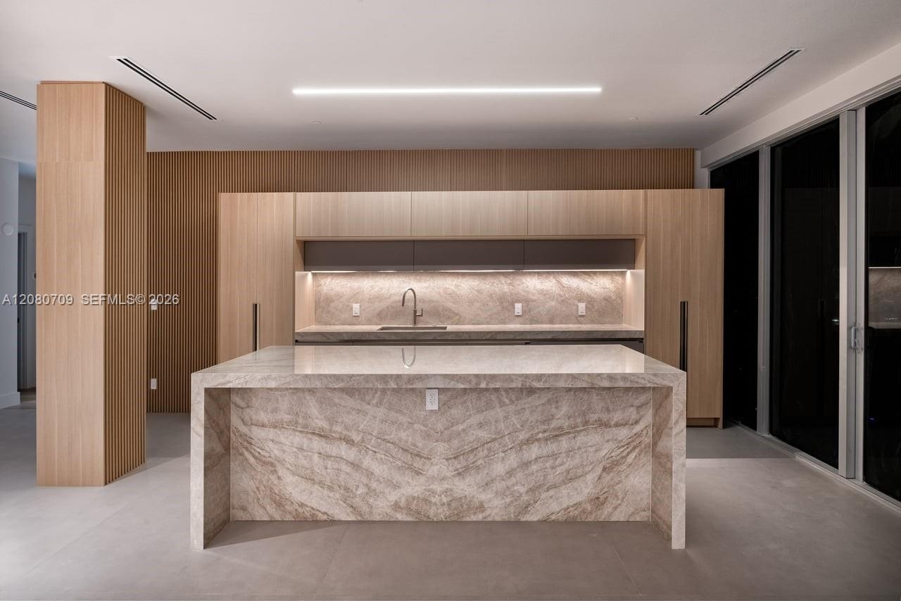 Open-concept interior featuring floor-to-ceiling windows, recessed lighting, wood-finish wall paneling, and a stone-clad kitchen island
