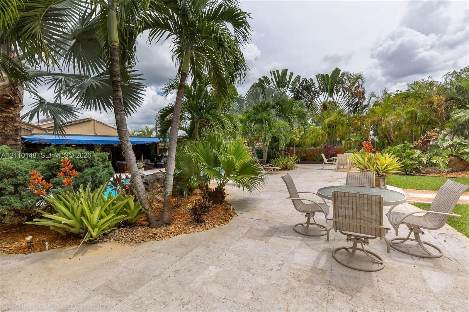 Expansive stone-paved patio featuring established palm trees, landscaped garden beds, and manicured lawn areas