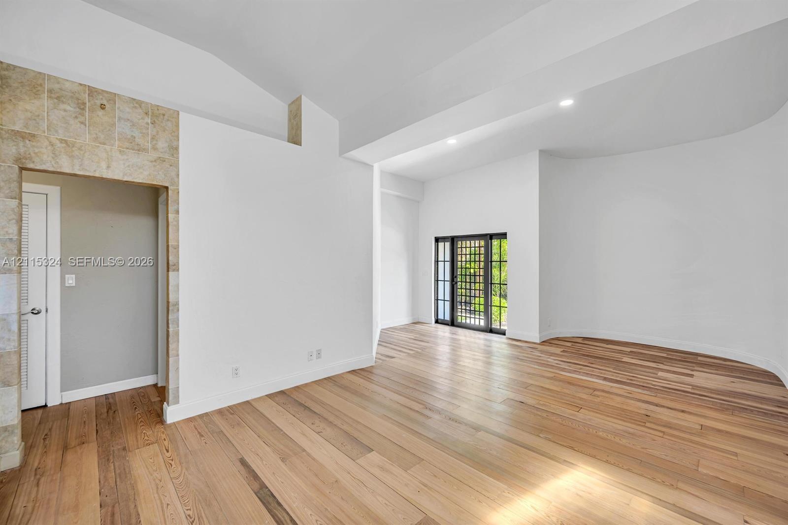 Interior featuring vaulted ceilings, wood-finish flooring, a curved wall, stone-accented doorway, and a multi-pane glass door