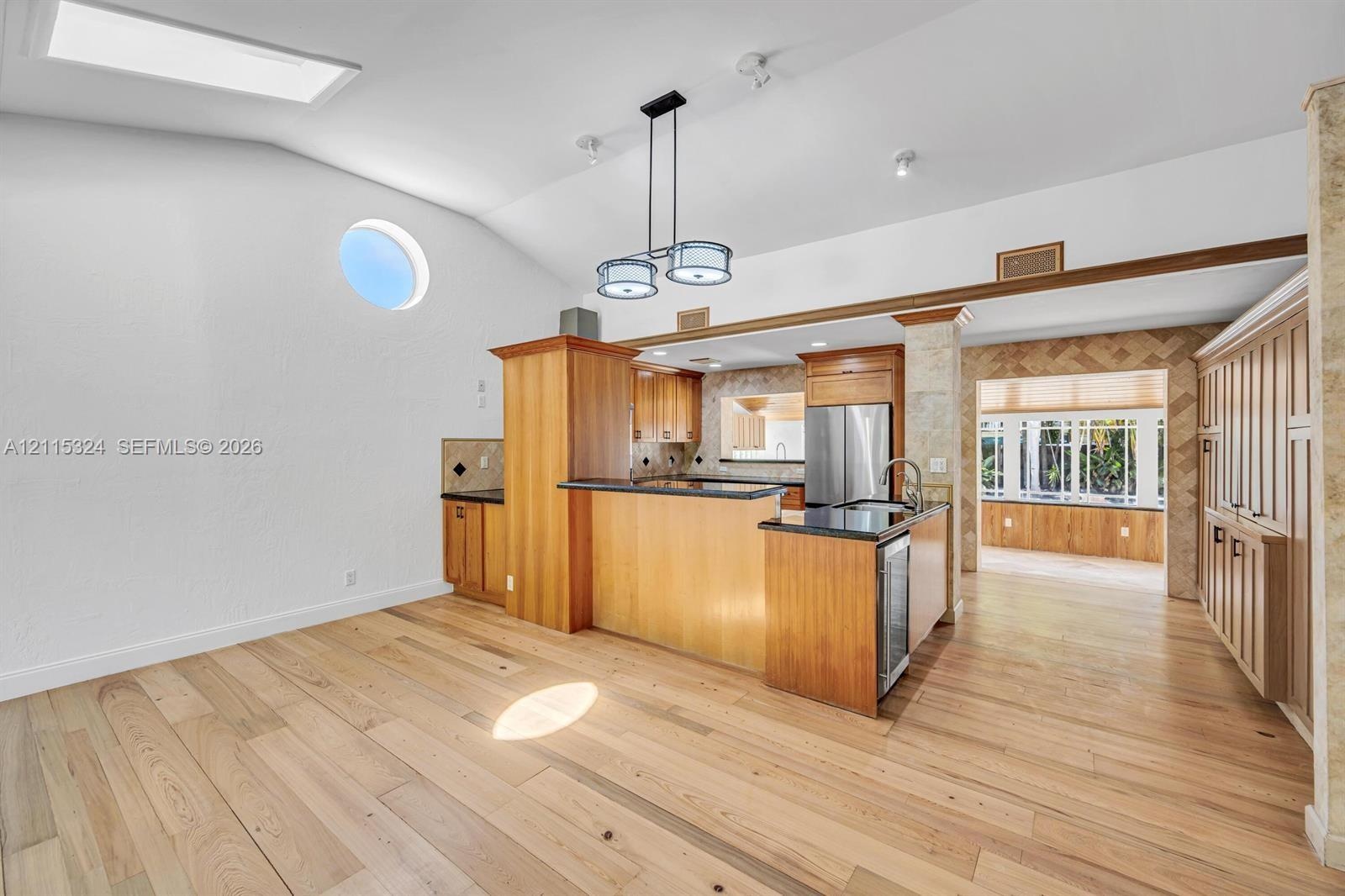 Vaulted ceilings featuring a skylight and circular accent window, wood-finish flooring, custom cabinetry with dark countertops, and a modern multi-pen