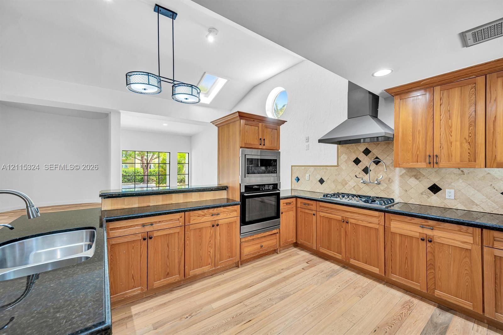 Kitchen featuring wood cabinetry, dark stone countertops, stainless steel appliances, a tiled backsplash with diamond accents, and a vaulted ceiling w