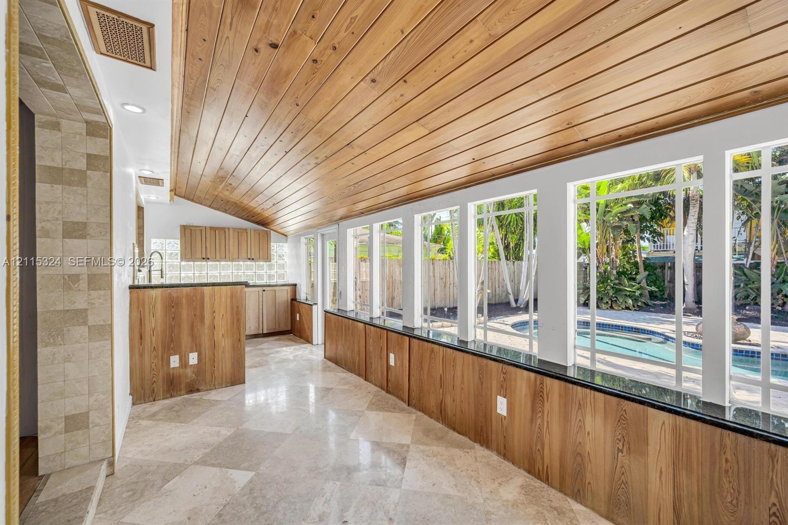 Vaulted wood-plank ceiling, stone tile flooring, built-in wooden cabinetry, custom millwork wall paneling with integrated stone countertops, and exten
