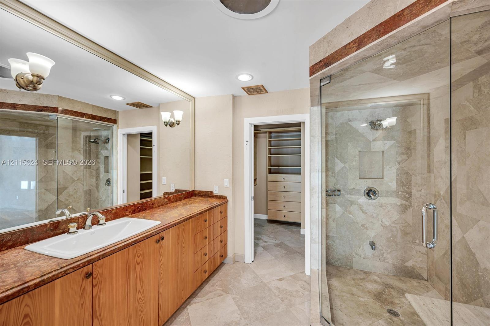 Bathroom featuring a stone-topped vanity with an integrated basin, expansive wall-mounted mirror, glass-enclosed shower with stone tile surround, and 