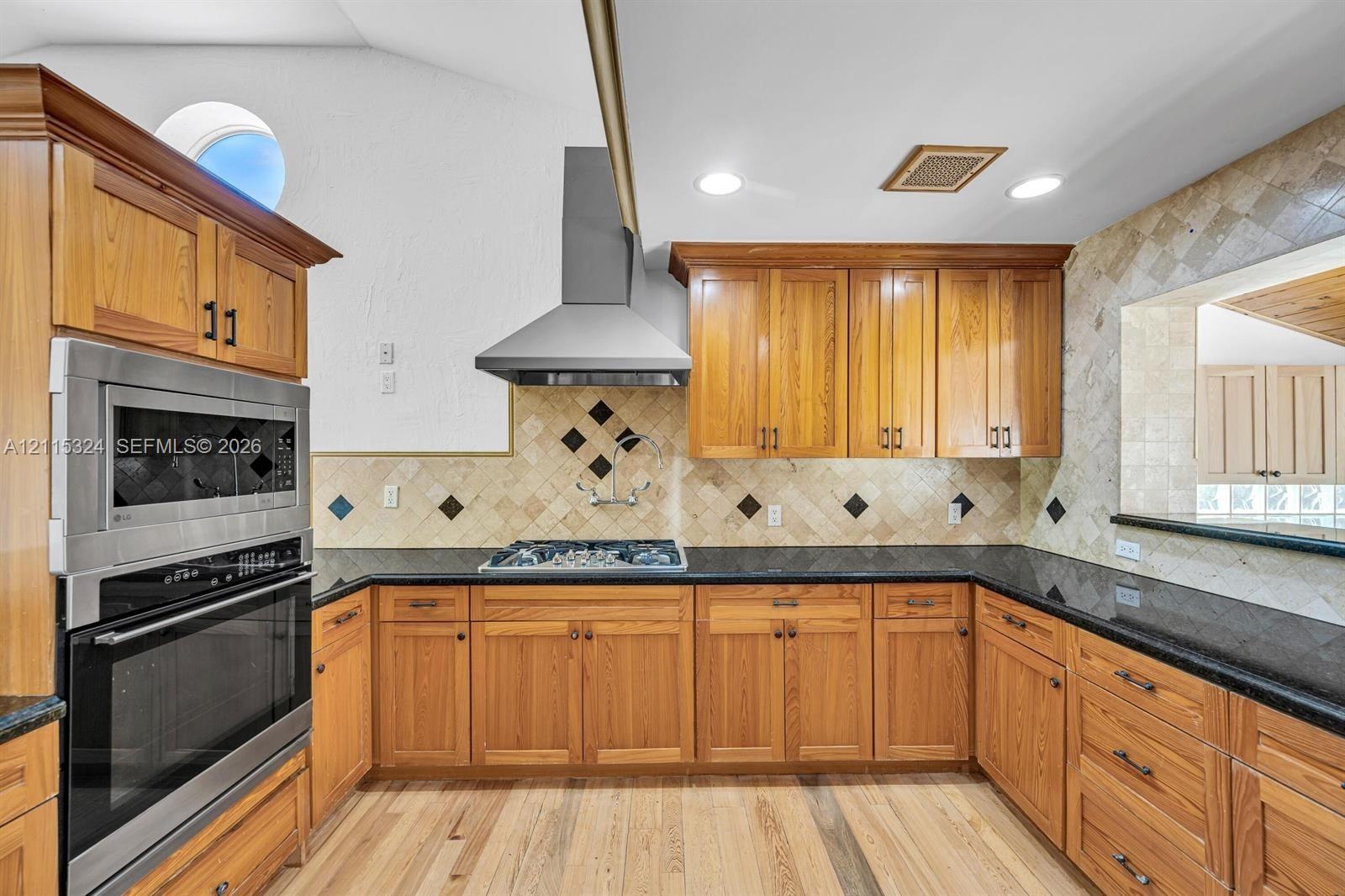 Kitchen featuring natural wood cabinetry, dark stone countertops, stainless steel wall-mounted oven and microwave, professional-style stainless steel 
