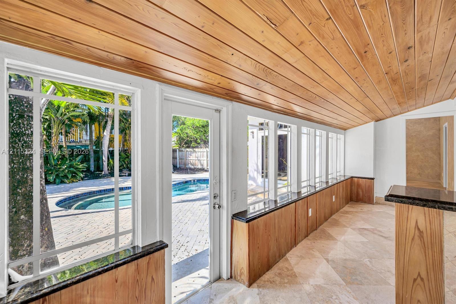 Sunroom featuring wood-plank ceiling, natural stone flooring, floor-to-ceiling windows, and built-in cabinetry with dark stone countertops