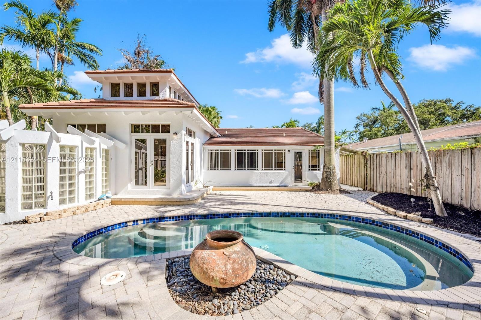Custom-designed outdoor area featuring a swimming pool, integrated fountain, paver stone hardscaping, tiered architectural roofline, and glass block p